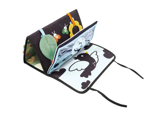 Tapis sensoriel d'éveil Hape plié en forme de triangle pour stimuler bébé pendant le jeu sur le ventre (tummy time), dévoilant un livre en tissu intégré avec un oiseau noir et blanc.