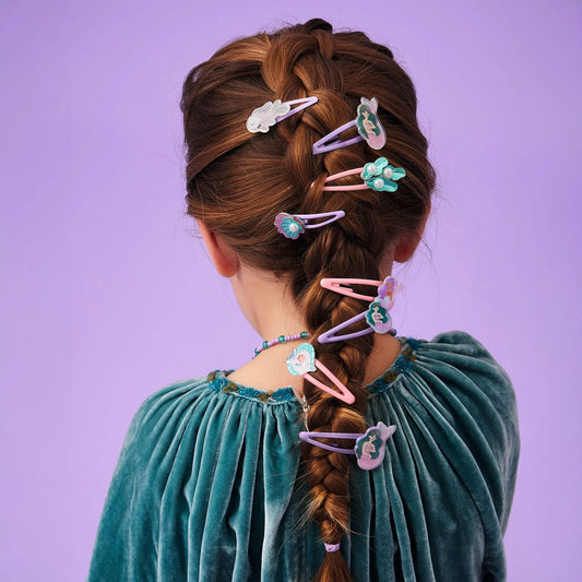 Jeune fille vue de dos avec une longue tresse française décorée de plusieurs barrettes à cheveux rose et violettes de la collection Plume par Djeco, sur le thème de la mer et des sirènes.