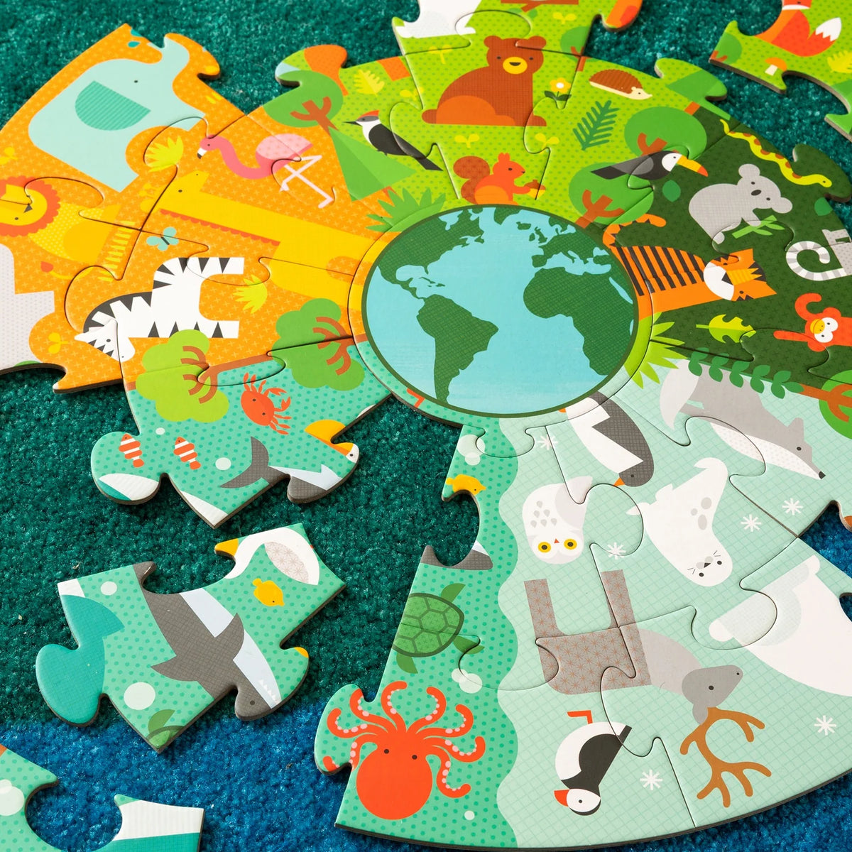 Assemblage en cours du casse-tête géant de sol Planète Terre 25 pièces Petit Collage sur un tapis vert.
