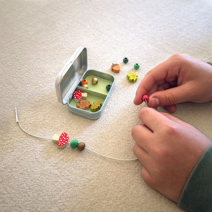 Mains d'un enfant en train d'enfiler des perles en bois colorées sur un cordon pour fabriquer un bracelet du kit Cotton Twist.