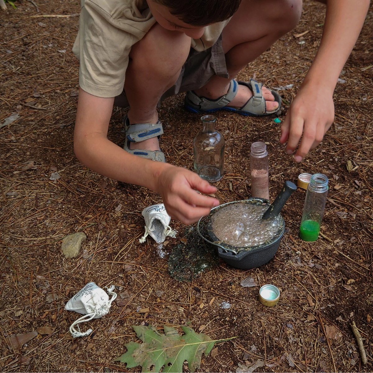 Enfant accroupi en extérieur mélangeant une potion magique effervescente dans un petit chaudron en fonte.