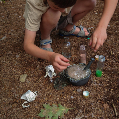 Enfant accroupi en extérieur mélangeant une potion magique effervescente dans un petit chaudron en fonte.