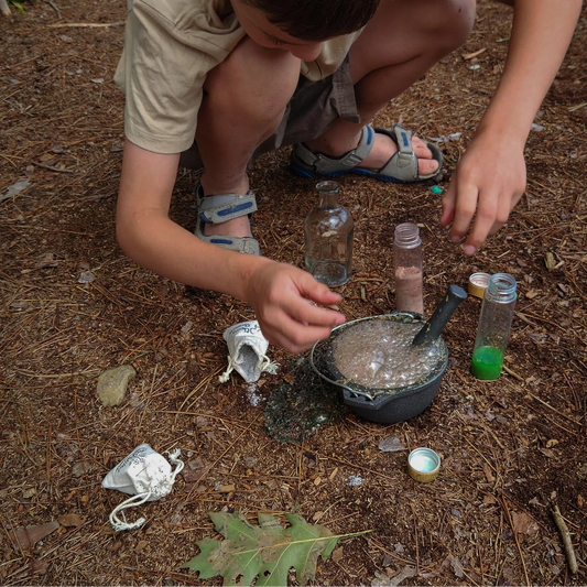 Enfant accroupi en extérieur mélangeant une potion magique effervescente dans un petit chaudron en fonte.