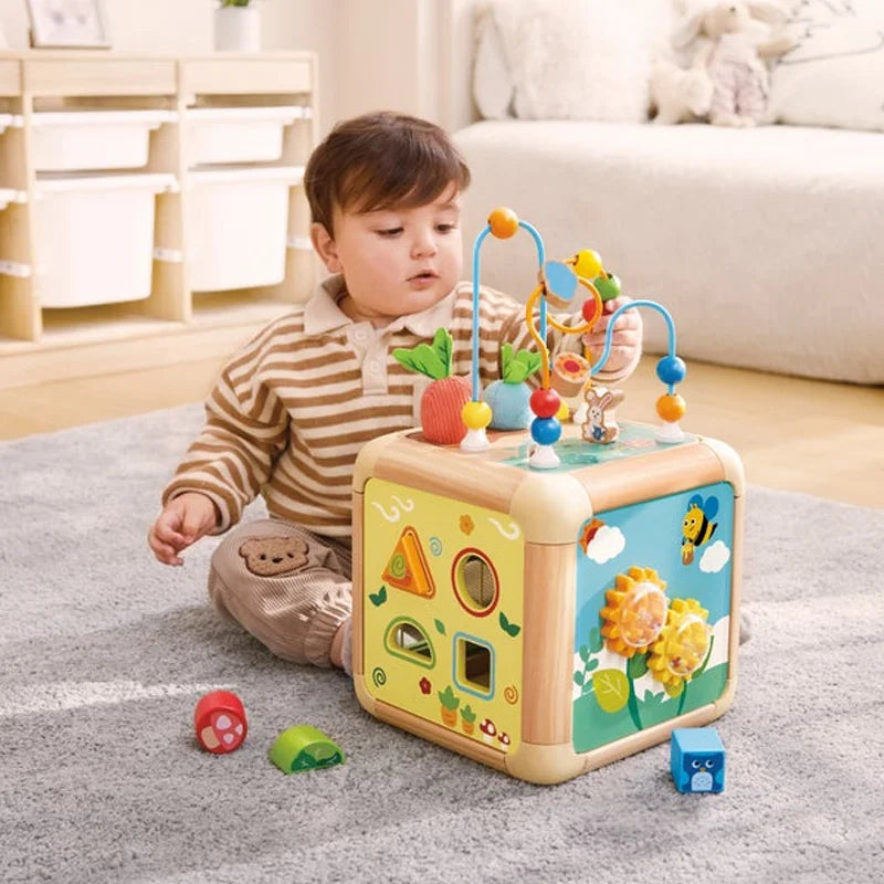 Bébé assis par terre jouant avec le labyrinthe de billes au sommet du cube d'activités en bois Hape.