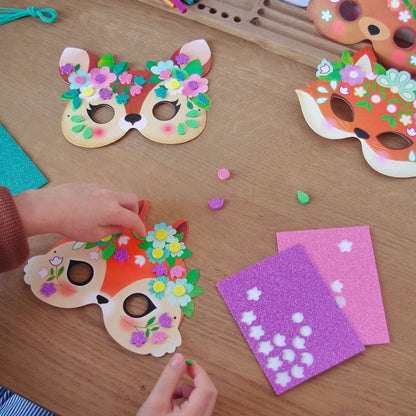 Enfant décorant des masques d'animaux de la forêt avec des mosaïques autocollantes pailletées de la collection Do It Yourself de Djeco.