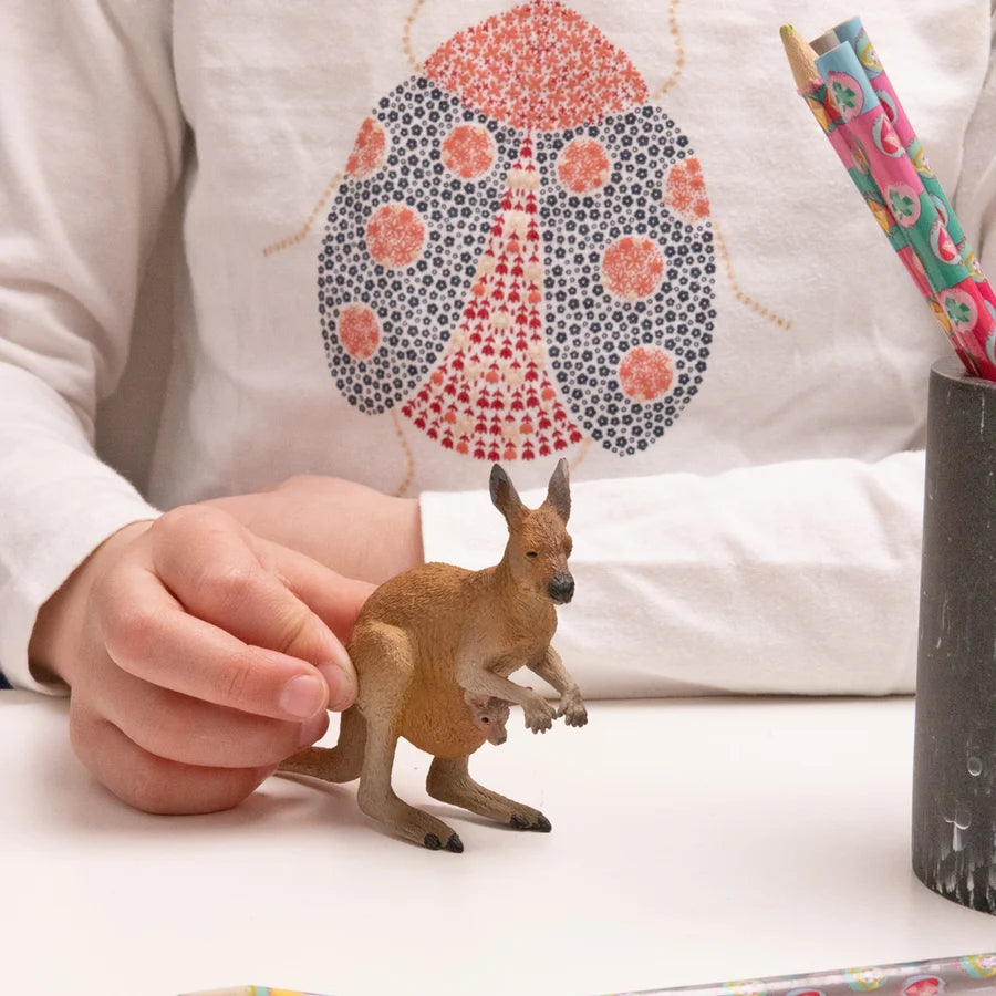 Figurine en plastique Kangourou et son bébé Papo peinte à la main, tenue sur une table par la main d'un enfant.