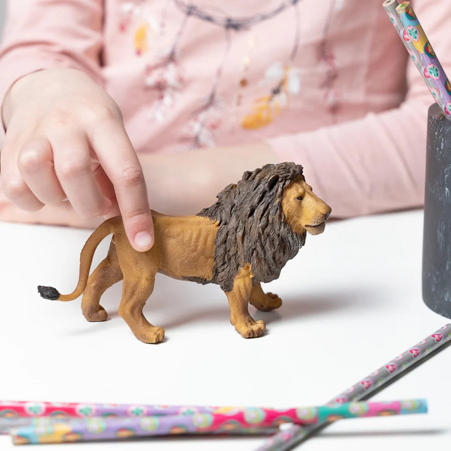 Figurine de lion majesteux Papo peinte à la main posée sur une table et tenue par la main d'un enfant.