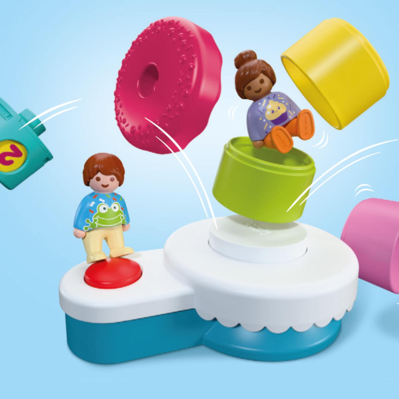 Illustration du fonctionnement du gâteau d'anniversaire Playmobil Junior 72086 projetant ses pièces colorées et figurines en appuyant sur le bouton rouge.