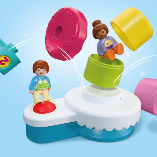 Illustration du fonctionnement du gâteau d'anniversaire Playmobil Junior 72086 projetant ses pièces colorées et figurines en appuyant sur le bouton rouge.