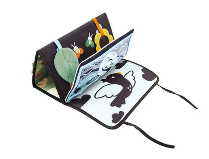 Tapis sensoriel d'éveil Hape plié en forme de triangle pour stimuler bébé pendant le jeu sur le ventre (tummy time), dévoilant un livre en tissu intégré avec un oiseau noir et blanc.