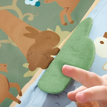 Gros plan sur la main d'un bébé touchant un élément texturé en tissu vert en forme de buisson sur le tapis d'éveil Hape.