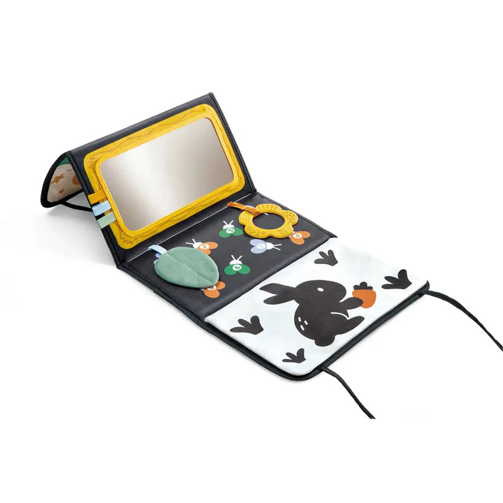 Tapis d'éveil pliable de la collection Hape x The Met ouvert au sol, montrant une section avec un miroir d'activité, des textures de feuilles, un anneau de dentition et une illustration contrastée de lapin noir et blanc.