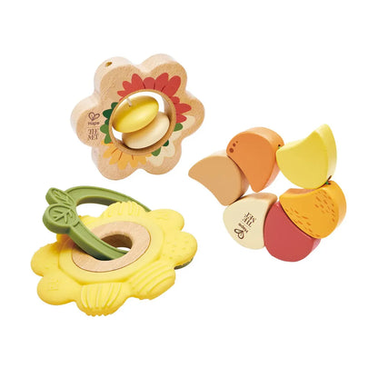 Détail des trois hochets d'éveil Hape x The Met comprenant un anneau de dentition fleur jaune, une marguerite en bois à billes et une fleur aux pétales articulés.