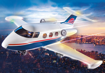 Avion jet privé de luxe Playmobil blanc et bleu en plein vol au-dessus d'une ville illuminée.
