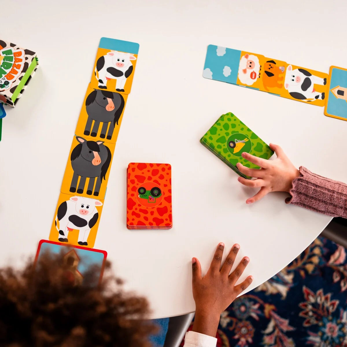 Enfants jouant autour d'une table au jeu de cartes Bazar à la ferme Nathan avec des alignements de cartes animaux.