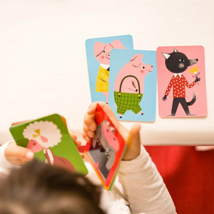 Enfant manipulant des cartes illustrées du jeu Le Mistigri Nathan sur une table avec des cartes de cochons et d'un loup posées.