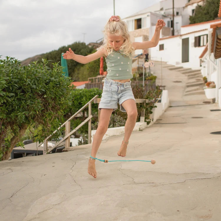 Jeune fille jouant à l'extérieur avec le jeu de cheville Ankle Swing en bois et corde turquoise de BS Toys.