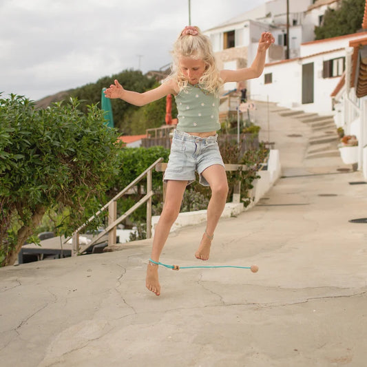 Jeune fille jouant à l'extérieur avec le jeu de cheville Ankle Swing en bois et corde turquoise de BS Toys.