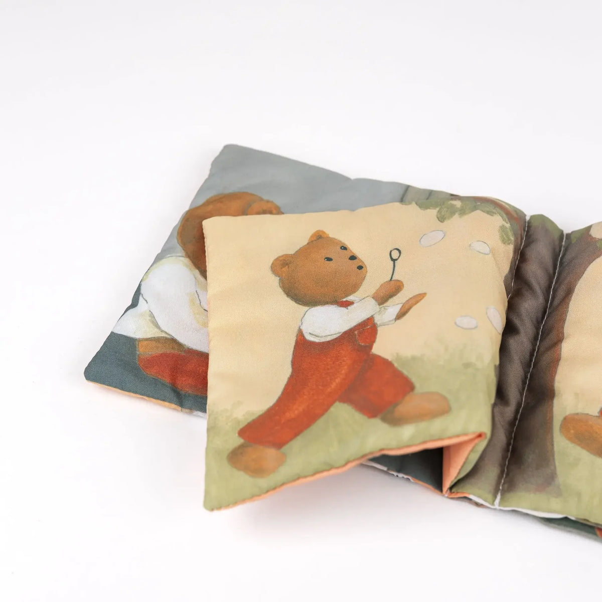 Page intérieure souple du livre en tissu Marcel l'Ours Egmont Toys illustrant un ourson en salopette rouge faisant des bulles.