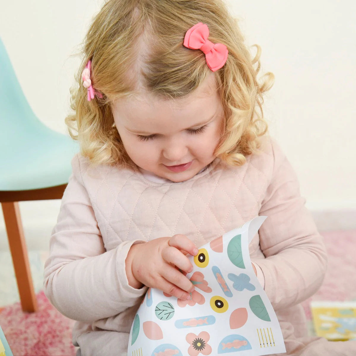 Gros plan sur une petite fille qui manipule une planche de gommettes géantes et colorées aux motifs de la nature (fleurs, poissons, feuilles) de l'activité créative Poppik pour les tout-petits.