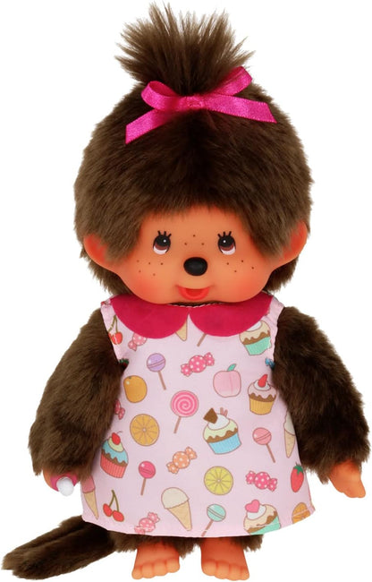 Peluche Monchhichi fille Pop 'N Candy Sekiguchi vêtue d'une robe rose imprimée de bonbons et gâteaux, avec un nœud fuchsia dans les cheveux.