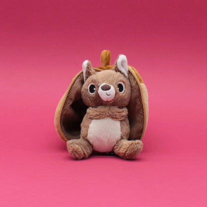 Peluche 2 en 1 Flipetz Les Déglingos représentant un écureuil brun sortant d'un gland en tissu sur fond rose.