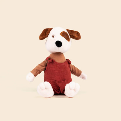 Peluche Eddie le chien de Egmont Toys, assis, avec une tache brune sur l'œil et vêtu d'une salopette rouge brique en gaze de coton.