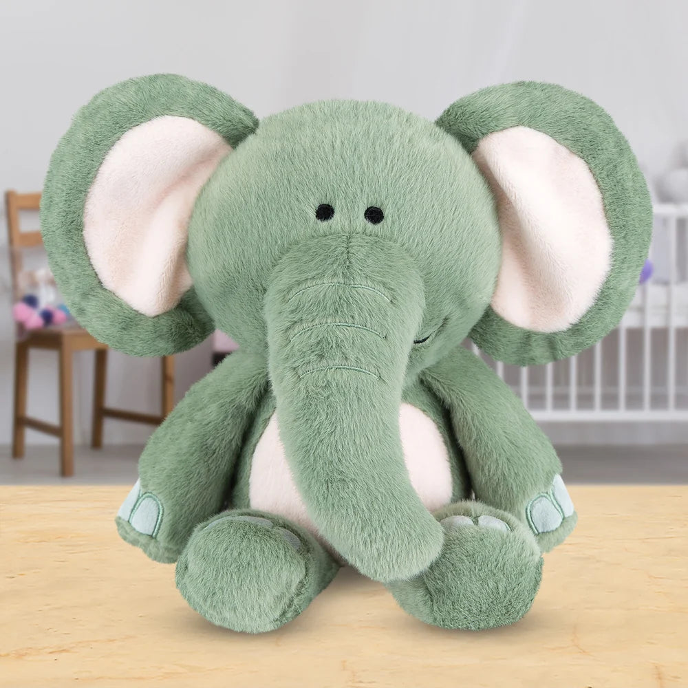 Peluche éléphant vert sauge aux grandes oreilles molletonnées et ventre rose doux, assise sur une table en bois, issue de la collection Zoo Crew.