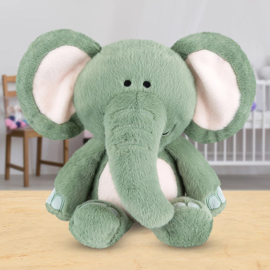 Peluche éléphant vert sauge aux grandes oreilles molletonnées et ventre rose doux, assise sur une table en bois, issue de la collection Zoo Crew.