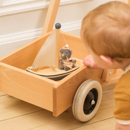 Enfant jouant avec le voilier en bois Egmont Toys et sa petite peluche chat Malo installés dans un chariot de marche.