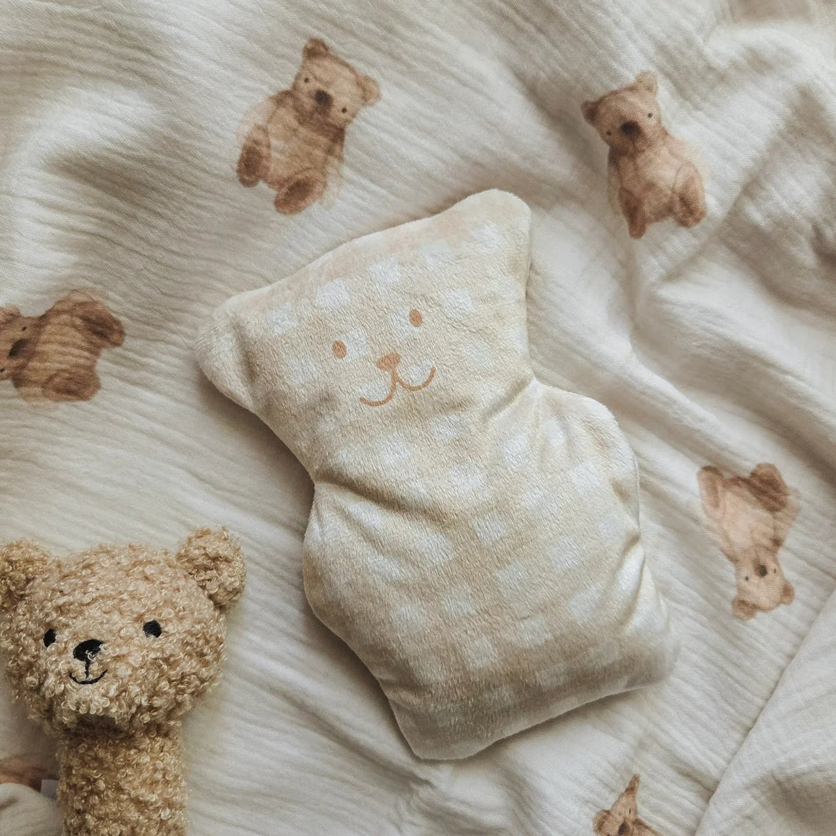 Petit ourson thérapeutique Béké Bobo imprimé vichy beige posé sur un tissu léger à motif d'oursons.