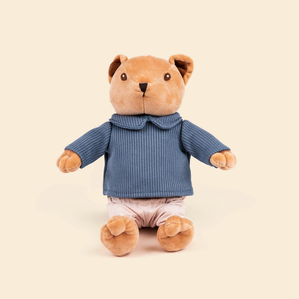 Peluche Alexis l'ourson de Egmont Toys, assis, vêtu d'un pull en tricot bleu à col et d'un petit pantalon rose pâle.
