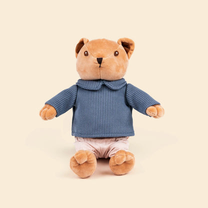 Peluche Alexis l'ourson de Egmont Toys, assis, vêtu d'un pull en tricot bleu à col et d'un petit pantalon rose pâle.