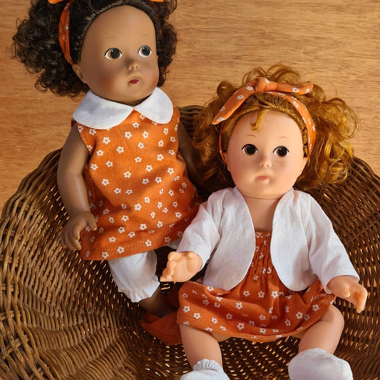 Deux poupées Egmont Toys habillées de tenues orange à motifs fleuris assises dans un panier en osier.