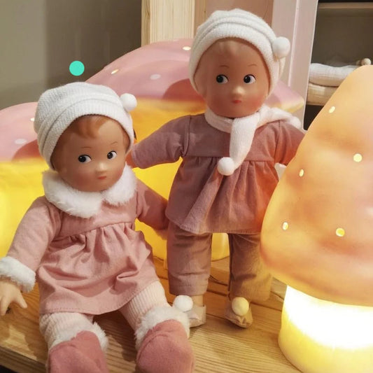 Deux poupées à jouer Egmont Toys habillées de tenues roses et de bonnet blanc posées à côté d'une lampe champignon lumineuse.