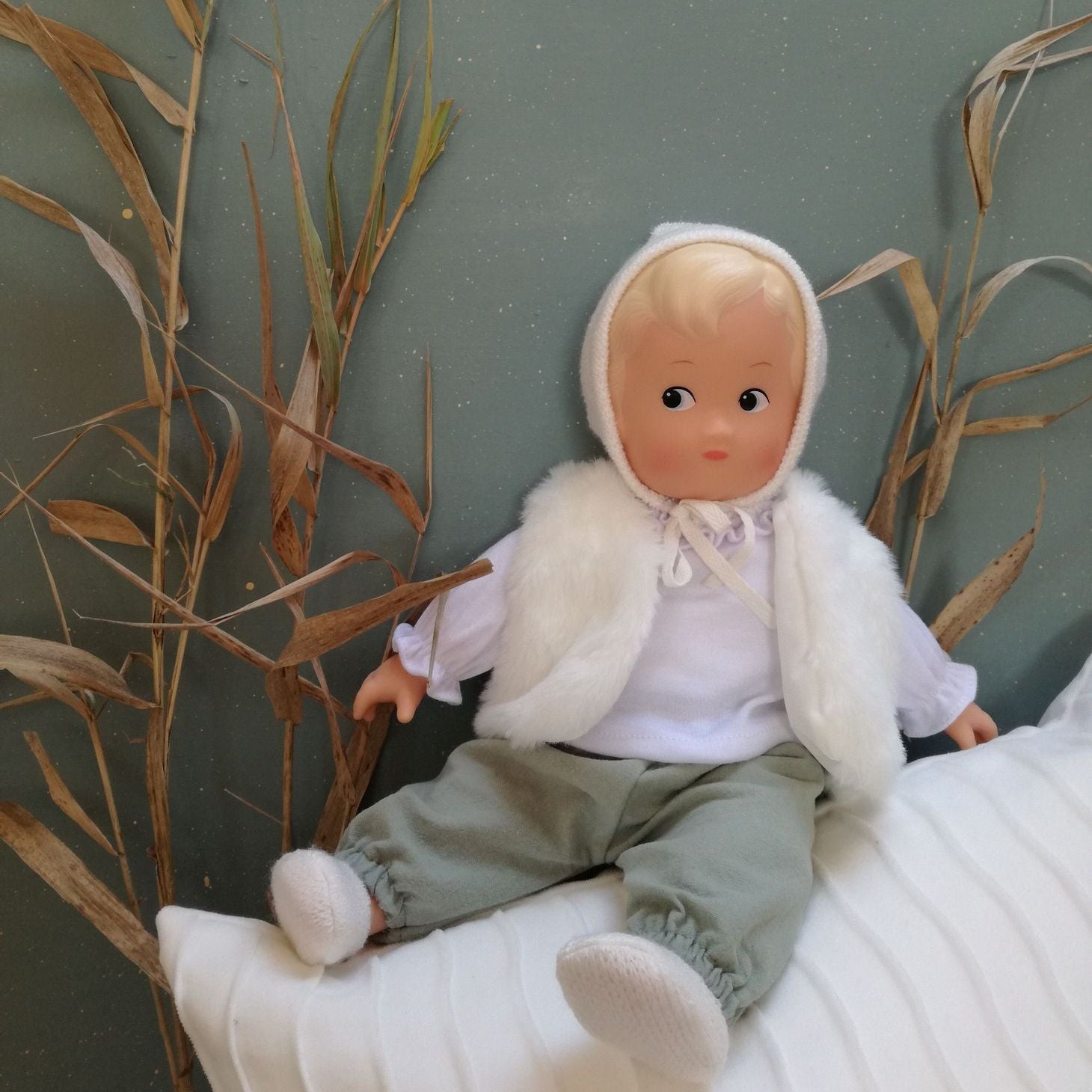 Poupon en vinyle Léa de la collection Les Petits Egmont Toys avec pantalon vert sauge et tenue d'hiver.