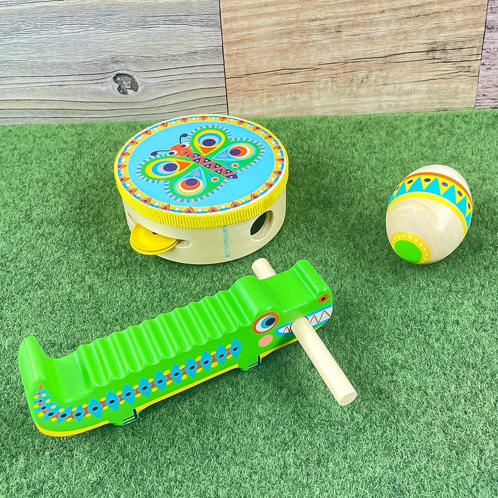 Enfilade d'instruments de musique en bois pour enfants Animambo de Djeco comprenant un tambourin papillon, une maracas œuf et un guiro crocodile vert sur fond d'herbe.
