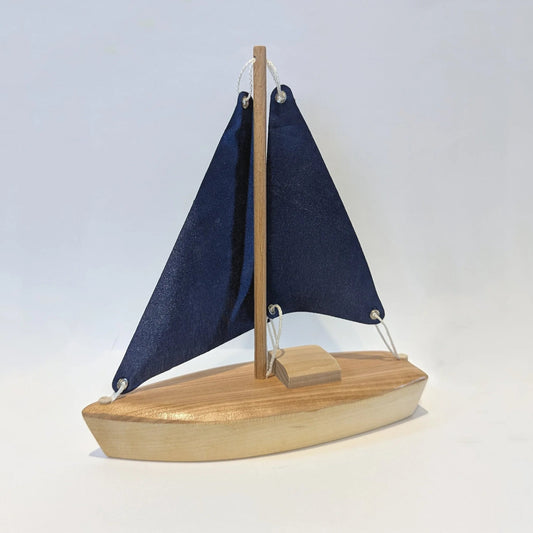 Petit voilier en bois artisanal Crocolo avec voiles bleues marines sur fond blanc.